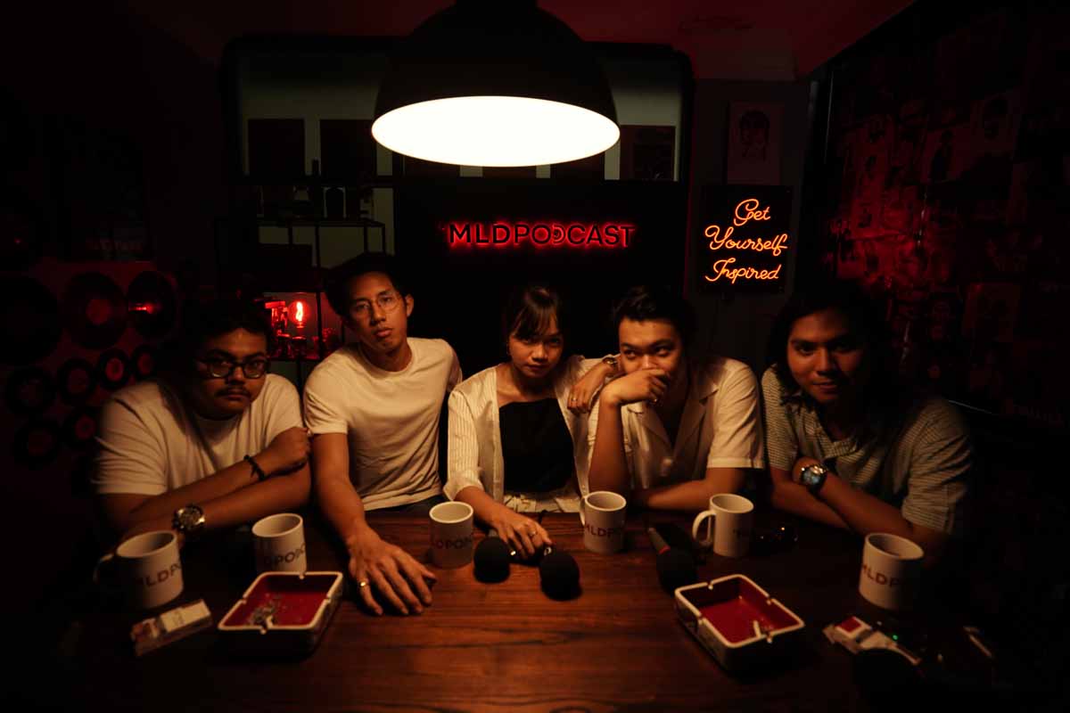 Reality Club berfoto dengan vibe lampu berwarna kuning dan background bertuliskan MLDSPODCAST
